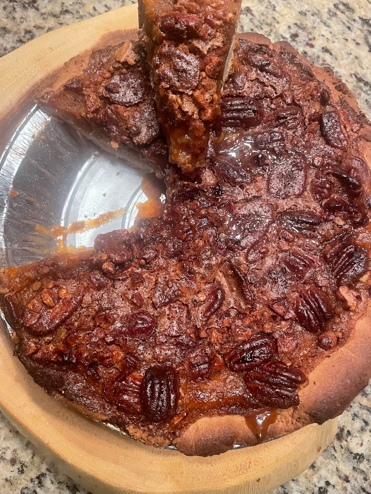 Delicious pecan pie with a caramelized top and a slice being served, showcasing the rich filling and crunchy pecans on a wooden plate.