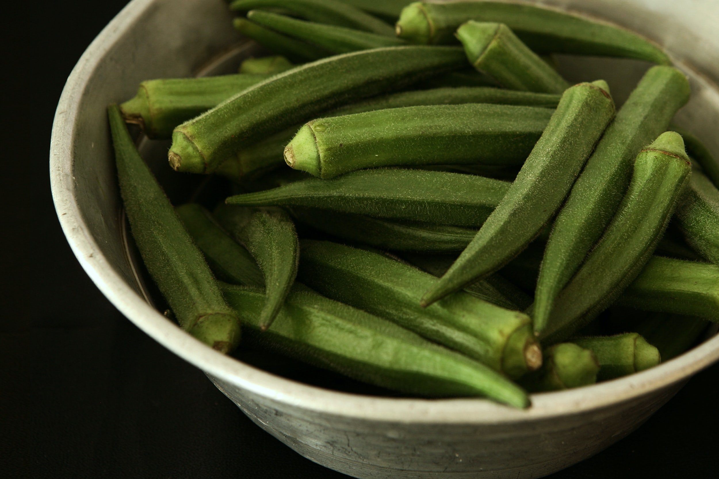 Fresh green okra pods arranged in a metal bowl, showcasing their smooth texture and vibrant color, ideal for healthy cooking and recipes.