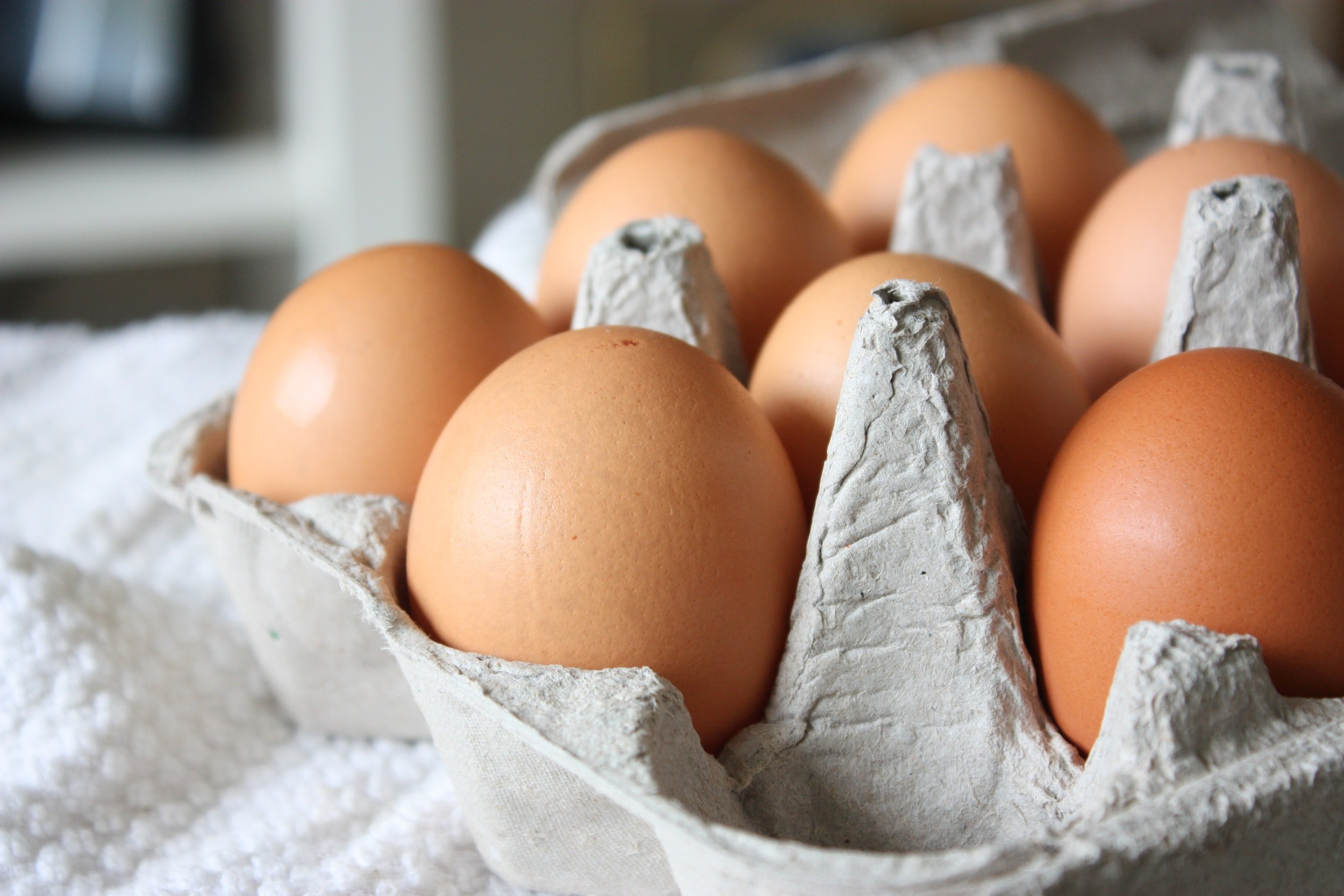 Fresh brown eggs arranged in a cardboard egg carton on a textured white cloth, highlighting their smooth surfaces and natural color.